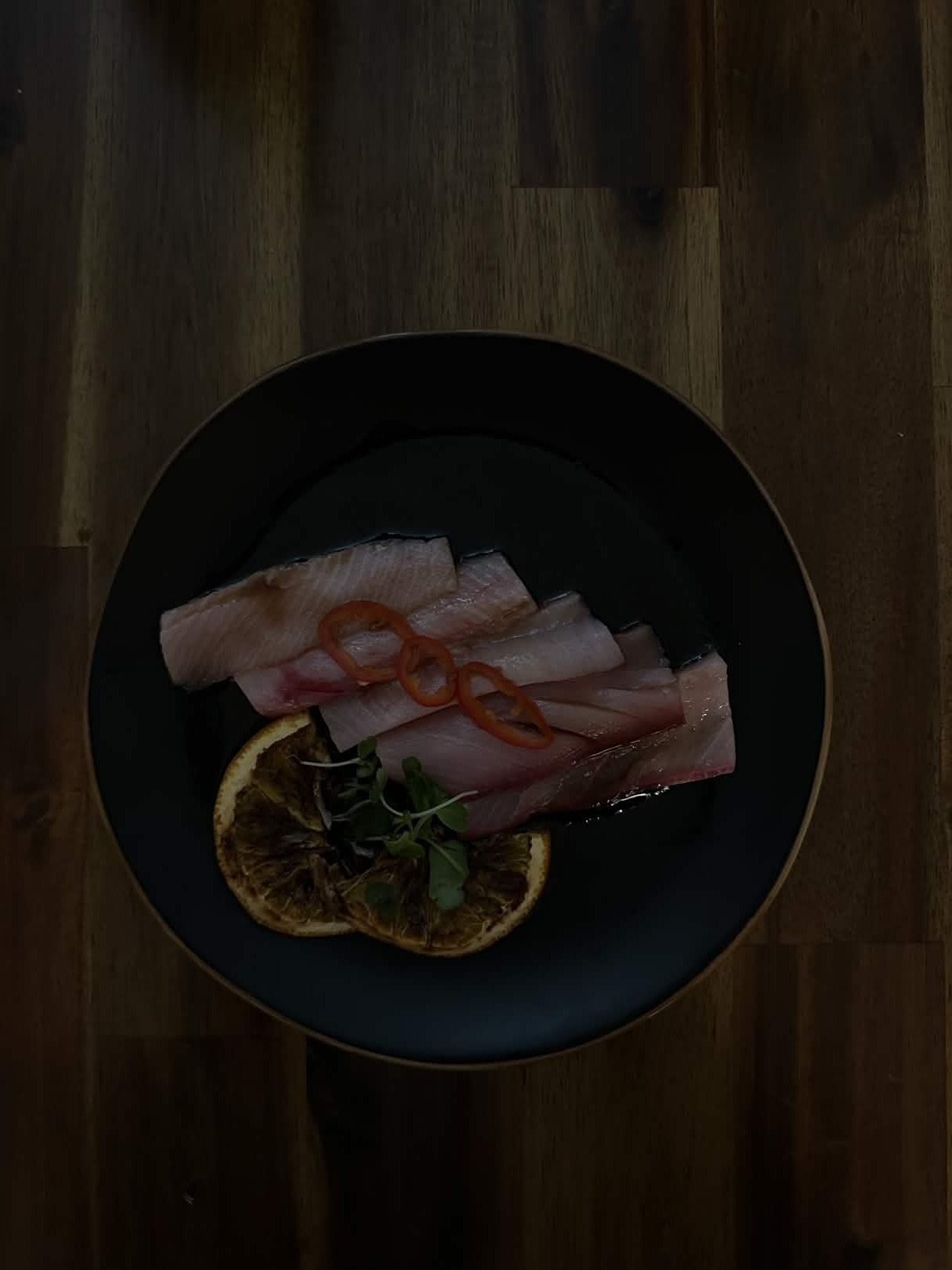 Hamachi loin crudo, garnished with pickled pepper slices, burnt lemon slices and sprouts