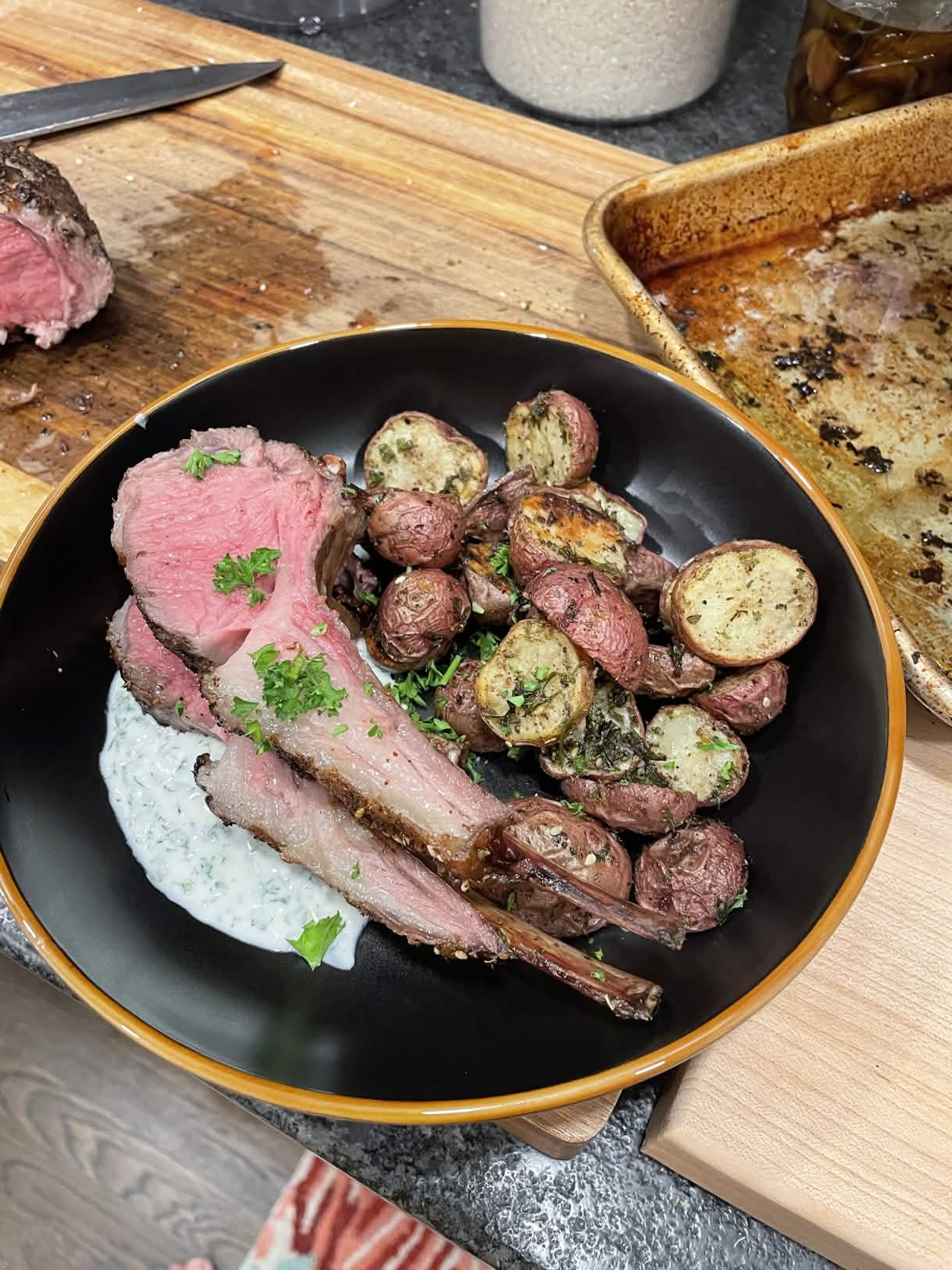 Lamb chops resting on yogurt sauce with a side of duck fat roasted potatoes, garnished with chopped parsley