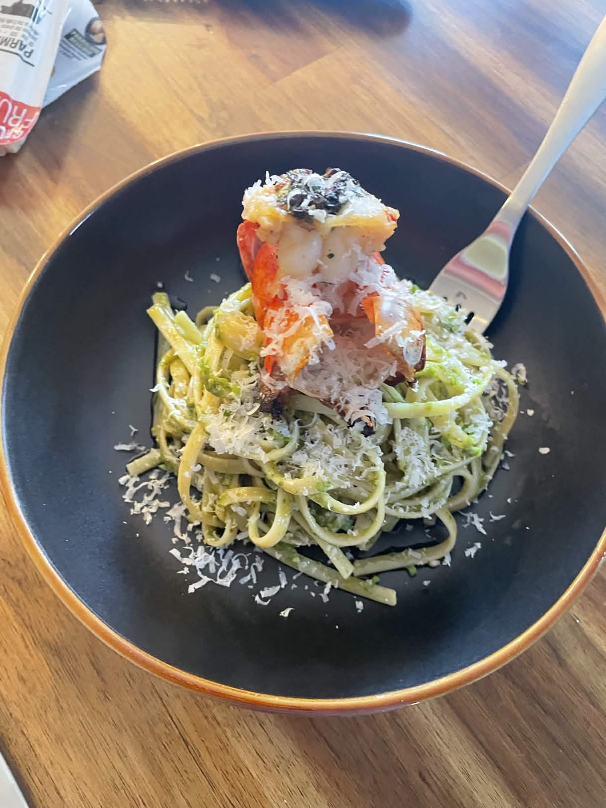Pasta dressed in pesto sauce and grated parmesan, and baked lobster tail on top